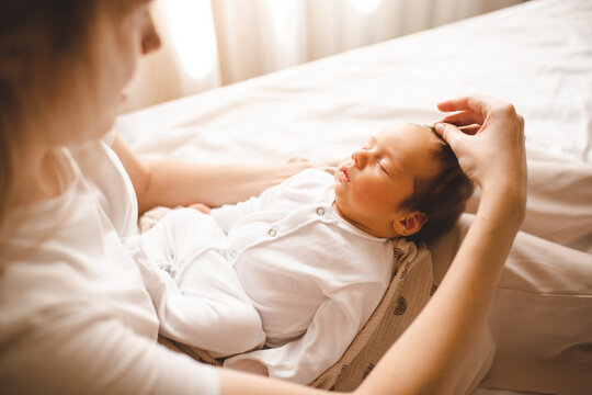 Woman holding sleeping baby boy touching his hair in ben on mother hands close up. Motherhood.
