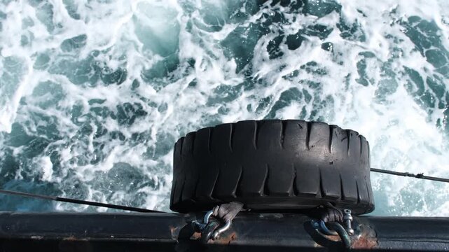 High angle view of black rubber tire fender on boat side over turbulent splashing sea foam waves   