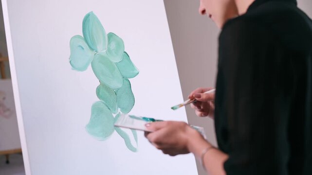 The artist paints a picture. A woman applies paint to a canvas with a brush in the studio.