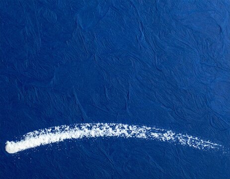 White chalk pigment curving low across deep indigo blue paper with large copy space