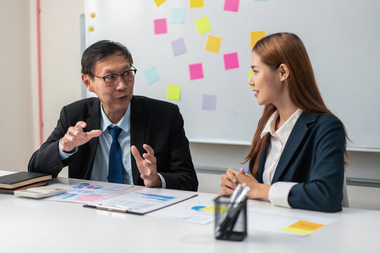 Two people in suits are talking at a desk