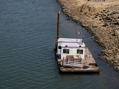 Rusty Work Barge with Cabin Moored Along Rocky Riverbank