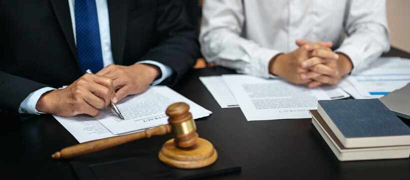 Two men are sitting at a desk with papers and a gavel