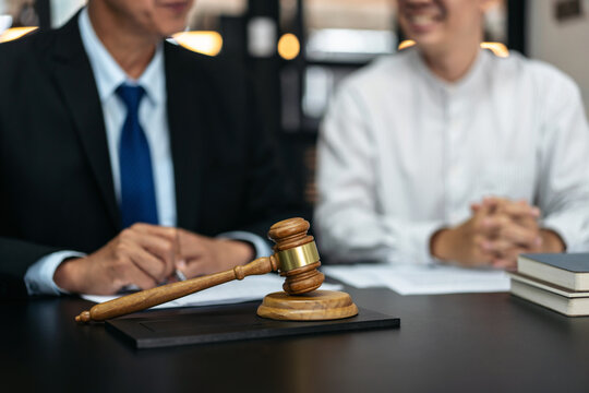 Two men are sitting at a table with a gavel in front of them