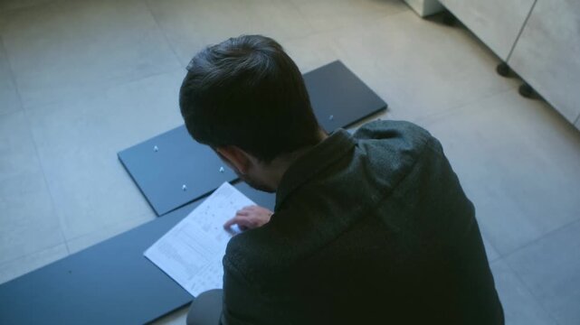 Top view man sitting on floor, reading assembly manual to build do it yourself flat pack furniture for new home during renovation project. Diy concept. Man assembling furniture following instructions
