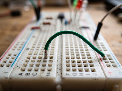 Green jumper wire connecting two points on electronic breadboard for circuit training.