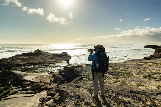 female photographer overlooking elevated view of massive wave sets rolling into Walker Bay Nature Reserve, South Africa 
