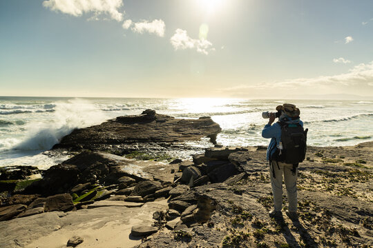 female photographer overlooking elevated view of massive wave sets rolling into Walker Bay Nature Reserve, South Africa 