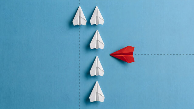Concept of individuality and leadership featuring a single red paper plane flying in a different direction from white planes