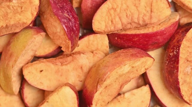 Rotating freeze-dried apple pieces shot in top-down macro close-up under bright studio light. Porous pale yellow dried fruit pieces fill the full frame.