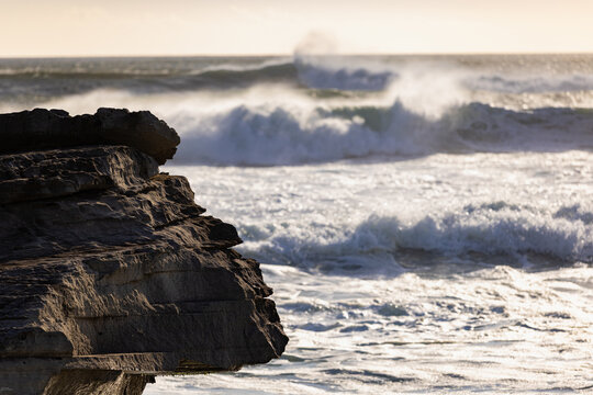 massive waves crashing into rock formations, Walker Bay Nature Reserve, South Africa at sunset.