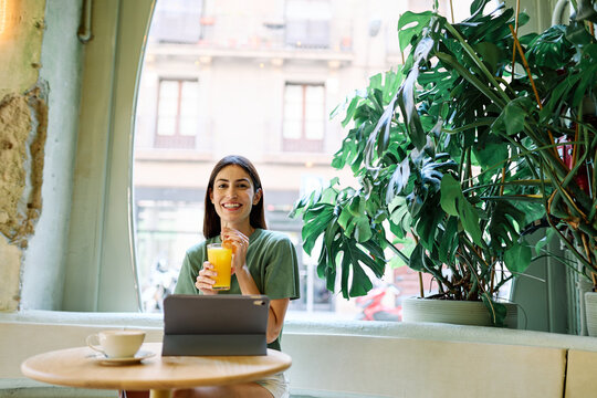 Portrait of a young woman girl  sitting in cafeteria or coffee shop drinking coffee or cappuccino and using a tablet computer  in the city and having fun