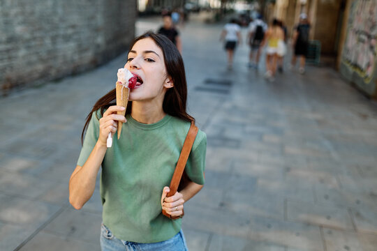 Portrait of a smiling young woman girl eating an ice cream walking in the city, tourists visiting destination, summer trip exploring