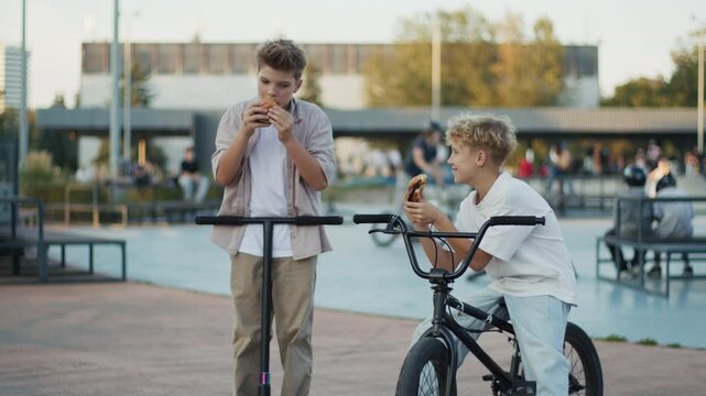 Two Boys Laughing and Eating Burgers in Skate Park
