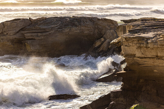 solo female photographer/hiker overlooking cliff with view you massive waves reaching Walker Bay Nature Reserve beach, South Africa at sunset