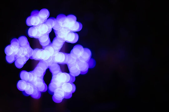 Defocused blue glowing snowflake on dark background, horizontal frame with space for text