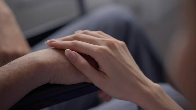 A person holds the hand of an elderly family member in a gesture of care and emotional support, conveying empathy, love, and compassion during a visit at home.