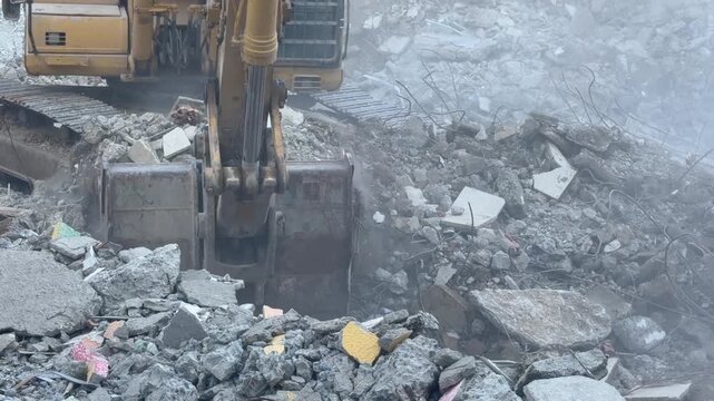 Industrial excavator bucket digs through broken concrete. Demolition machine pushes into piles of rubble and trash, lifting debris in gray cloud during site clearance with forceful mechanical motion.