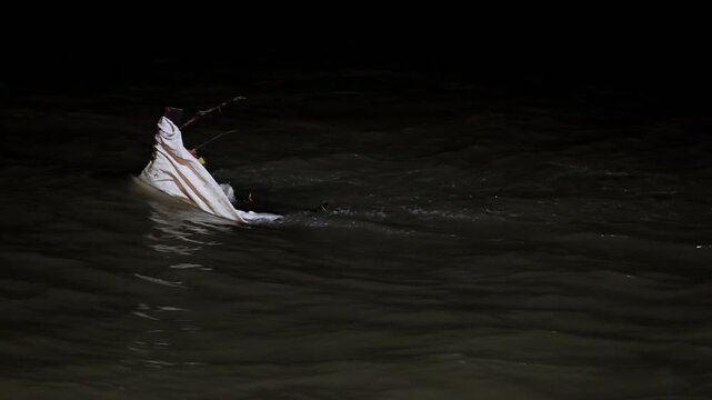 Pale fabric caught on a protruding branch shifts in the dark flowing Ganga River in Rishikesh at night.