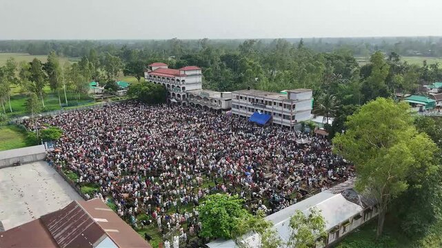 Large crowd of people gathered in a field for outdoor event near school buildings aerial view.
