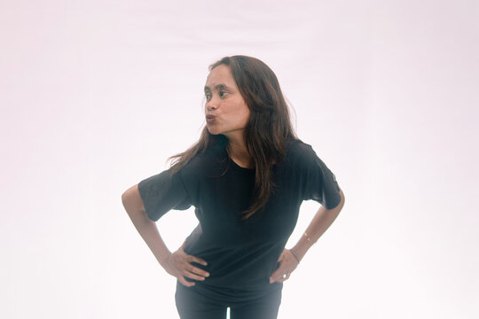 Portrait of a playful Asian woman in a black t-shirt posing with hands on hips and pouting face on a white backdrop.
