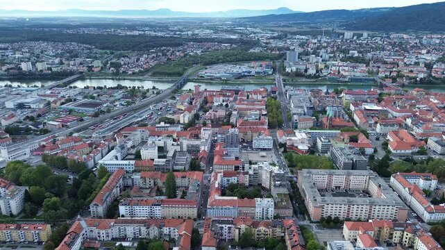 Top-down aerial view of central Maribor, Slovenia, showing historic buildings with red tiled roofs, tree-lined streets, courtyards and urban architecture.
