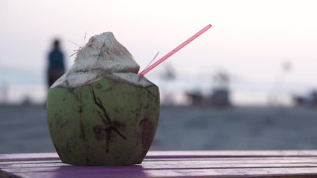 Fresh Coconut Drink with Straw on Wooden Table at Parang Tritis Beach, Yogyakarta