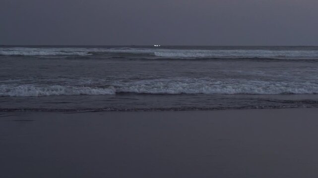 Ocean waves at Parang Tritis Beach, Yogyakarta, Indonesia. Seascape at sunset or dusk with dark water and sky, featuring breaking foamy waves on the shore.