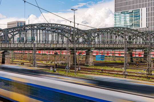 Motion blur of fast passenger train passing through busy urban railway junction with steel arch bridge and modern architecture, European public transport and mobility concept