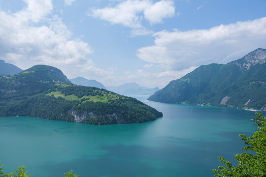 Spectacular wide panoramic view over the turquoise waters of Lake Lucerne (Lac des Quatre-Cantons) surrounded by green alpine ridges under a bright partly cloudy sky, showcasing pure Swiss serenity