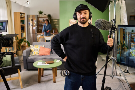 Portrait of young adult Caucasian sound operator holding boom microphone on film set during video production. Ideal for filmmaking courses, media production marketing, broadcasting concepts