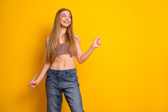 Attractive young woman holding a measuring tape and smiling in a casual outfit against a vibrant yellow background