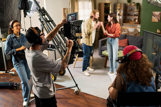 Film crew shooting scene with Caucasian actors on studio set using professional video camera equipment. Useful for media production and backstage cinematography campaigns