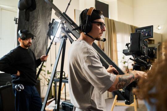 Young adult Caucasian videographer operating professional movie camera on jib arm in studio. Film crew creating media content for commercial video production advertising