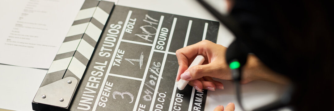 Caucasian young adult woman writing on clapperboard preparing scene for film production, close up. Useful for cinema industry, video marketing and media production