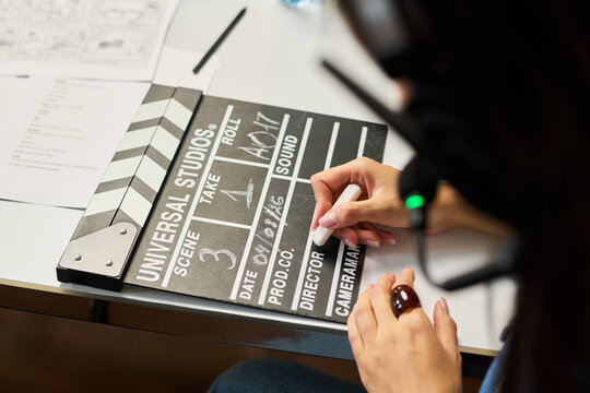 Young adult woman writing scene details on movie clapperboard during film production. Concept represents filmmaking industry, useful for cinema advertising and video production campaigns