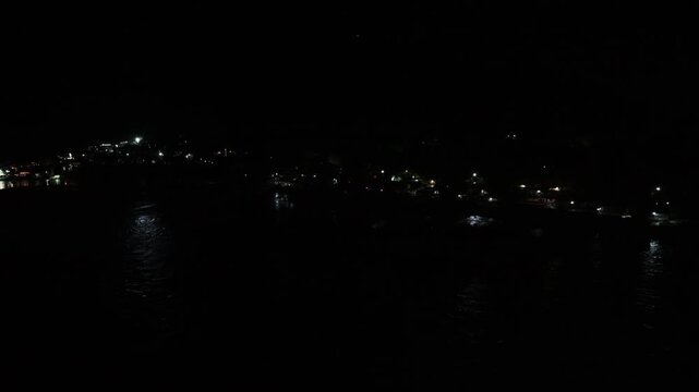 Riverfront and hillside lights shimmer on the Ganga River beneath dark slopes in Rishikesh at night.