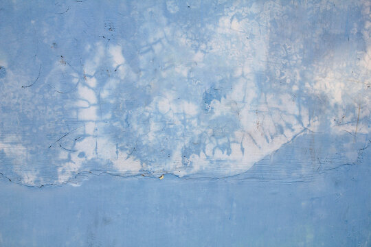 Cool blue tones dominate this weathered wall. White patches swirl as paint fades and peels. Cracked surfaces hint at age and exposure. The texture feels rough, yet calm and subdued