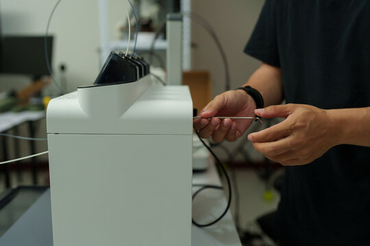 The focus is on the hands of a technician setting up a 3D printer to print a clear white plastic model, using cutting-edge technology and concentrating on specific points within the laboratory.