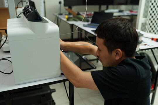 The focus is on the hands of a technician setting up a 3D printer to print a clear white plastic model, using cutting-edge technology and concentrating on specific points within the laboratory.