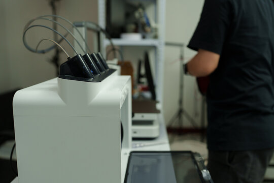 The focus is on the hands of a technician setting up a 3D printer to print a clear white plastic model, using cutting-edge technology and concentrating on specific points within the laboratory.