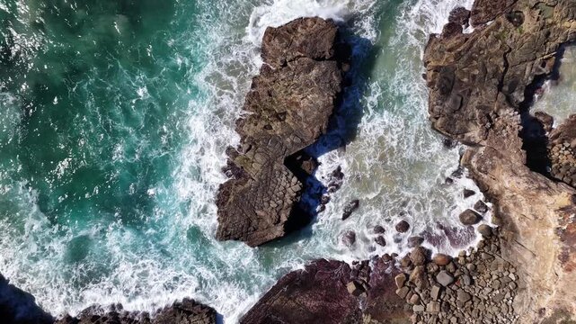 Aerial video looks straight down as waves break over rugged rock formations along the Yamba coastline, creating shifting patterns of white surf and blue water.