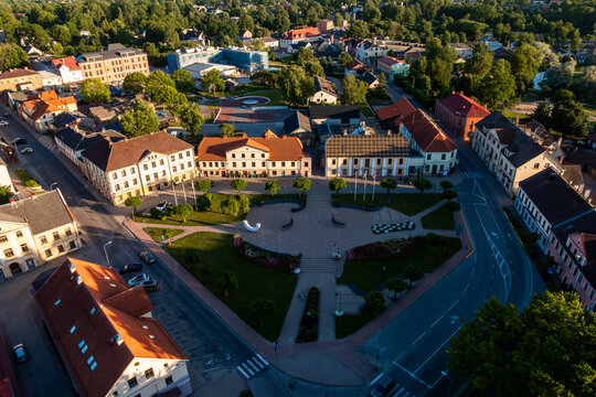 Saldus town square from above with flower beds, Latvia. High angle summer evening drone view of renovated Saldus town square, Latvia: paved plaza, lawns, flower beds, stairs, benches, white sculpture.