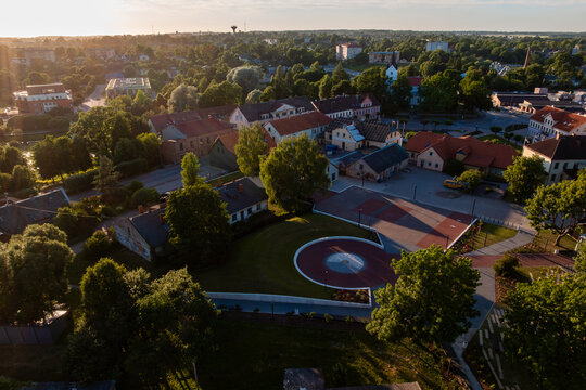 Modern circular plaza in Saldus town center, Latvia. Golden hour aerial of modern circular red plaza in historic Saldus town center, Latvia, with green lawn, benches, trees, old houses.