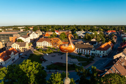 Copper rooster weathervane above Saldus town square, Latvia. Golden copper rooster weather vane on church steeple tip in warm evening sun, close drone perspective. Saldus town plaza in Latvia.