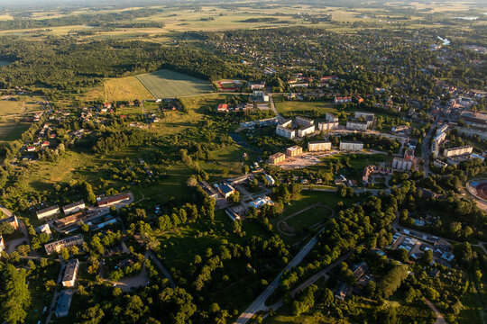Town outskirts with apartment blocks, forest and fields from above. Summer evening aerial of small town outskirts with apartment blocks, school, sports track, private houses, roads, green meadows.