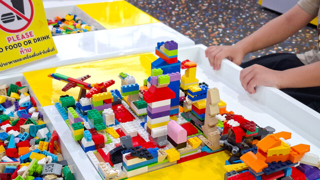 Child hands building colorful lego city towers and plastic brick structures on yellow play table at indoor playground on September 22, 2026 in Bangkok, Thailand.