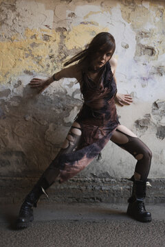Expressive lunge of woman against cracked wall, contemporary dance, post-apocalyptic costume