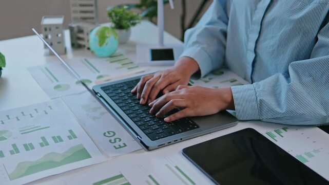Businesswoman reviewing ESG reports and green business financial charts with a laptop and documents. ESG concept Environmental, Social, and Governance, eco-friendly green building, sustainable
