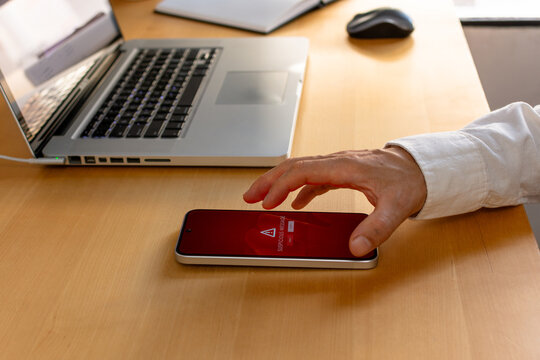 Smartphone security warning on wooden desk with hand reaching to device